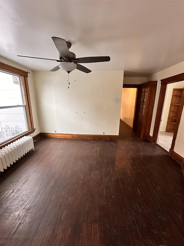 spare room with radiator, ceiling fan, baseboards, and dark wood-type flooring