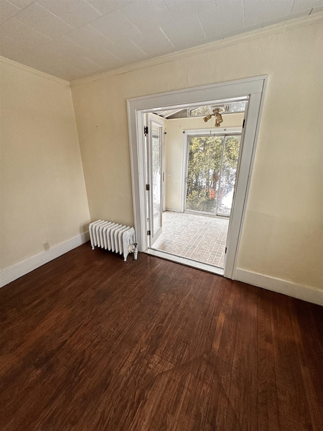 empty room with dark wood-type flooring, ornamental molding, radiator heating unit, and baseboards