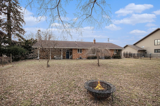 rear view of house featuring an outdoor fire pit, brick siding, fence, a yard, and a chimney