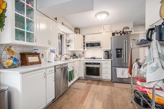 kitchen featuring light wood-style flooring, white cabinetry, light countertops, appliances with stainless steel finishes, and glass insert cabinets