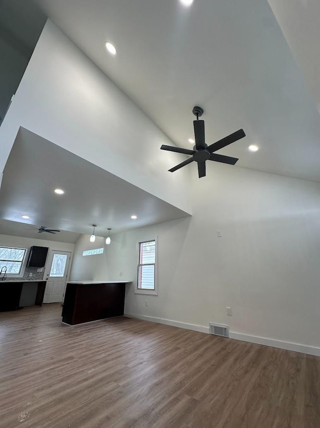 unfurnished living room with a ceiling fan, visible vents, baseboards, and wood finished floors