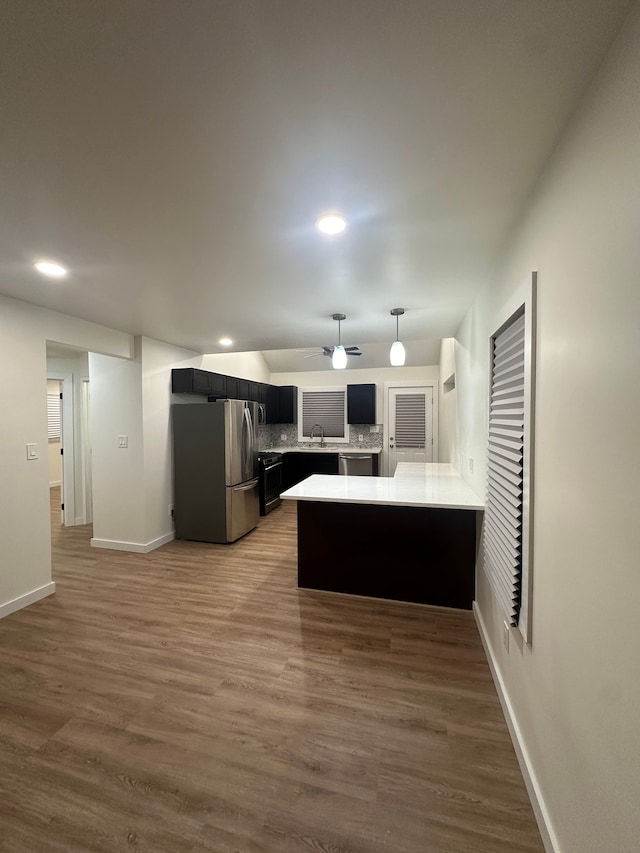 kitchen featuring tasteful backsplash, wood finished floors, a peninsula, stainless steel appliances, and a sink