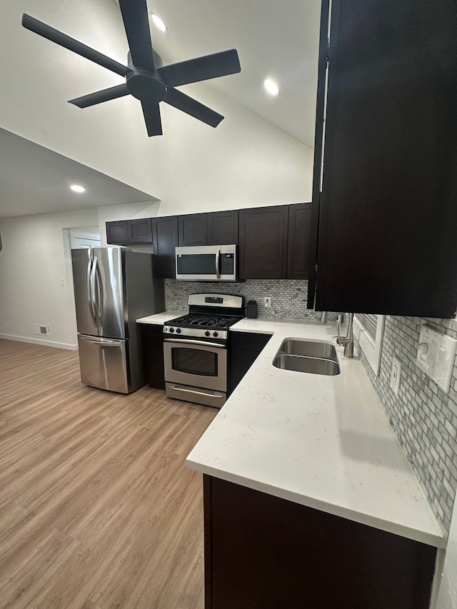 kitchen with dark cabinets, a sink, appliances with stainless steel finishes, light wood finished floors, and tasteful backsplash