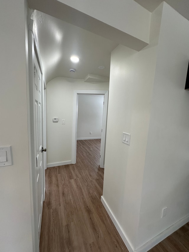 hall featuring dark wood-style floors, baseboards, and lofted ceiling