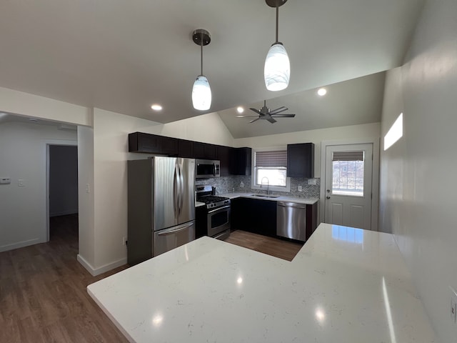 kitchen with stainless steel appliances, lofted ceiling, a sink, light stone counters, and backsplash
