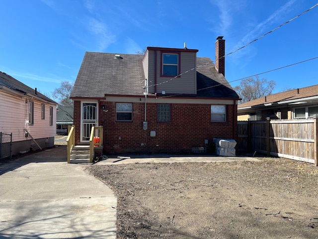 rear view of property with a chimney, fence, and brick siding