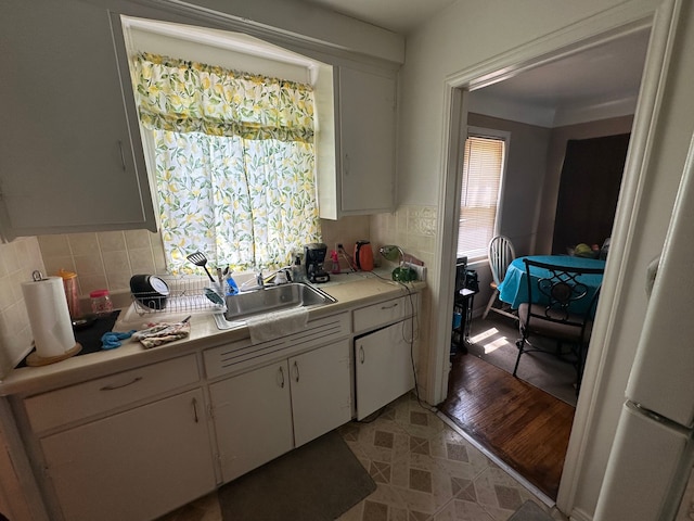 kitchen with light countertops, a sink, backsplash, and white cabinetry