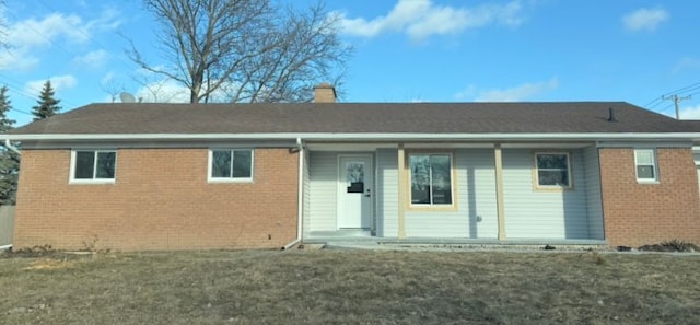 view of front facade featuring brick siding, a chimney, and a front yard