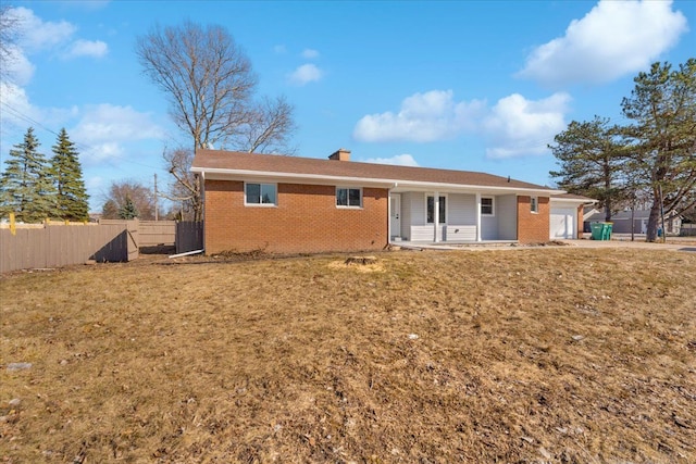 rear view of house with brick siding, fence, a chimney, a yard, and a garage