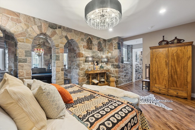 bedroom with arched walkways, recessed lighting, wood finished floors, and a notable chandelier