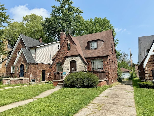 tudor home with a front lawn, a detached garage, brick siding, and a shingled roof