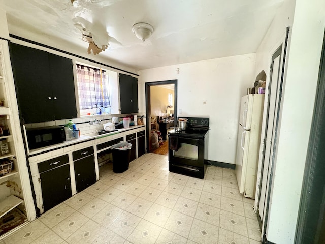 kitchen featuring tile countertops, dark cabinets, freestanding refrigerator, light floors, and black range with electric cooktop