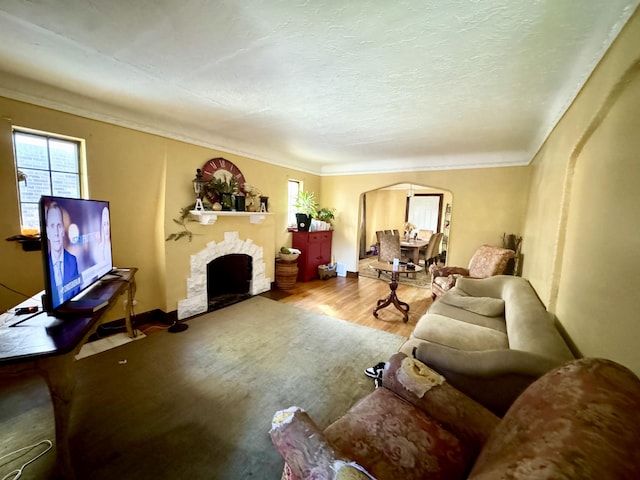 living area with arched walkways, a fireplace with flush hearth, ornamental molding, a textured ceiling, and wood finished floors