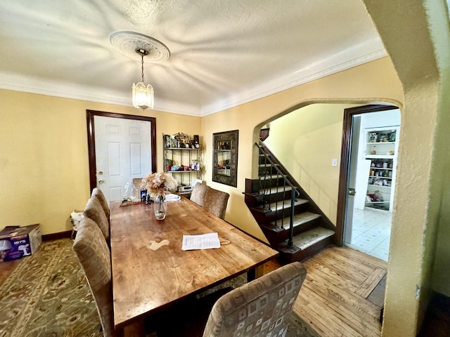 dining area featuring arched walkways, crown molding, stairway, and wood finished floors