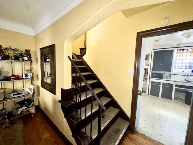 staircase featuring arched walkways, wood finished floors, and crown molding