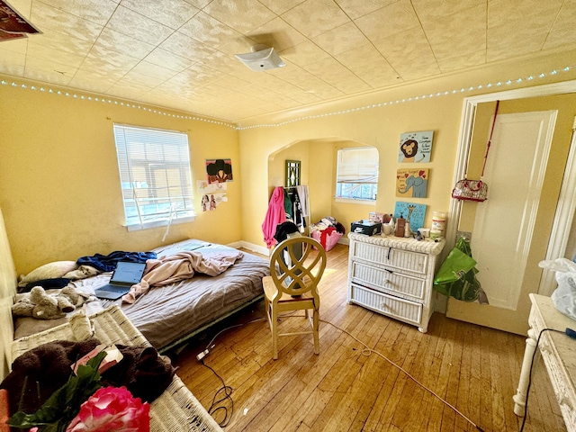 bedroom featuring arched walkways, hardwood / wood-style floors, multiple windows, and an ornate ceiling