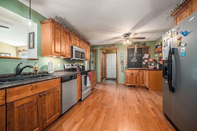 kitchen featuring light wood-style flooring, stainless steel appliances, a sink, brown cabinets, and dark countertops