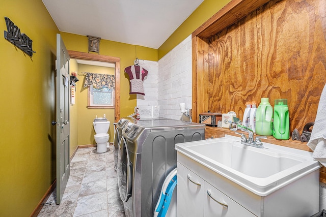 laundry room featuring laundry area, a sink, baseboards, stone finish flooring, and washer and clothes dryer