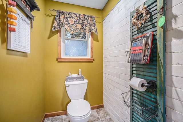 bathroom featuring baseboards, toilet, and brick wall