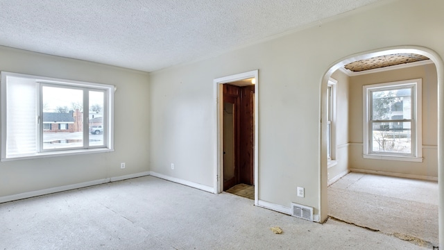 spare room featuring baseboards, visible vents, arched walkways, and a textured ceiling