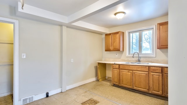 kitchen featuring light countertops, visible vents, brown cabinetry, a sink, and baseboards