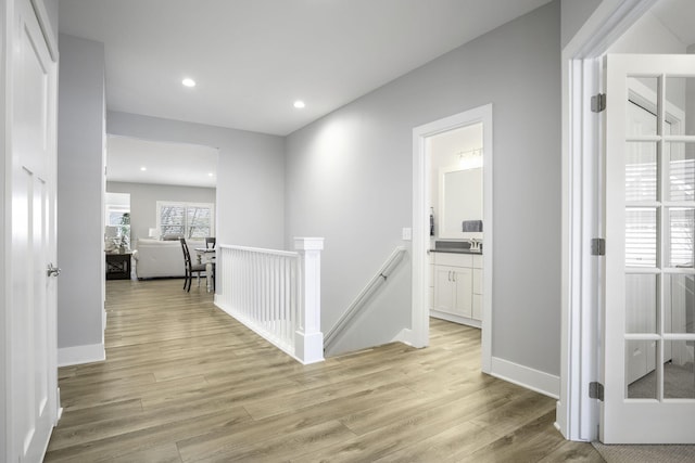 corridor featuring light wood-style floors, recessed lighting, baseboards, and an upstairs landing