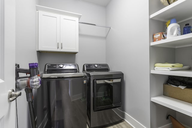 clothes washing area with cabinet space, light wood-style flooring, baseboards, and washer and dryer