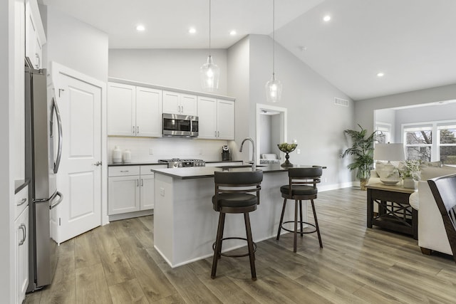 kitchen featuring visible vents, appliances with stainless steel finishes, a kitchen breakfast bar, wood finished floors, and a sink