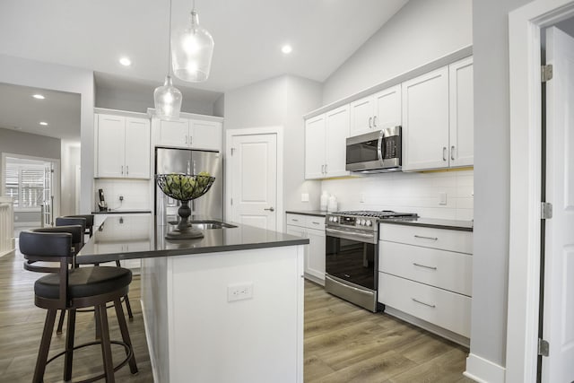 kitchen with a breakfast bar, decorative light fixtures, stainless steel appliances, dark countertops, and light wood-style flooring