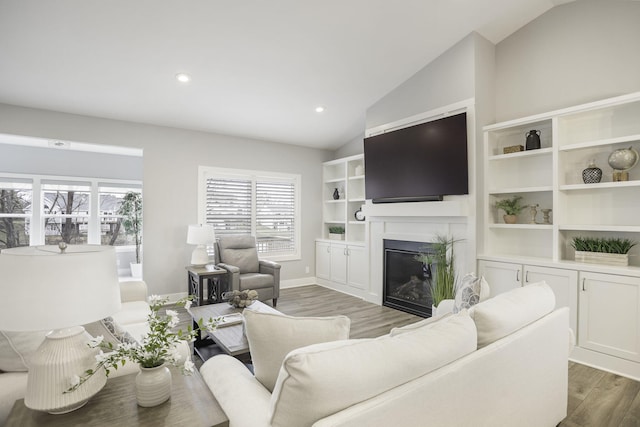 living area featuring lofted ceiling, recessed lighting, a glass covered fireplace, wood finished floors, and baseboards