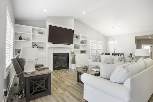 living room featuring a glass covered fireplace, light wood-style flooring, an inviting chandelier, vaulted ceiling, and recessed lighting