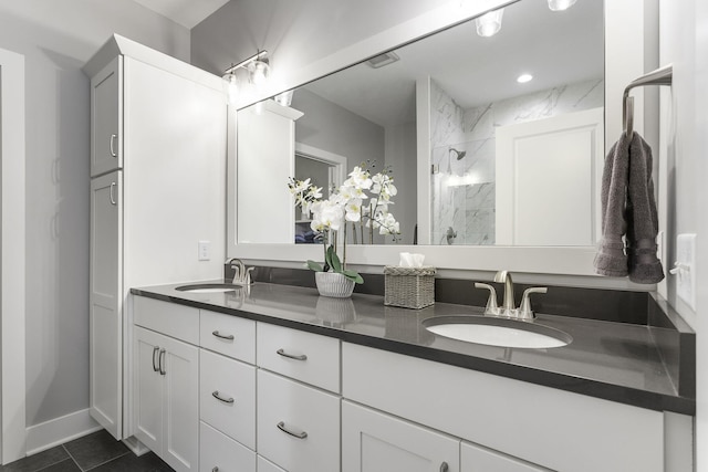 bathroom featuring double vanity, a marble finish shower, baseboards, and a sink