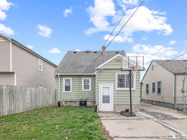 rear view of house with central air condition unit, a shingled roof, fence, driveway, and a lawn