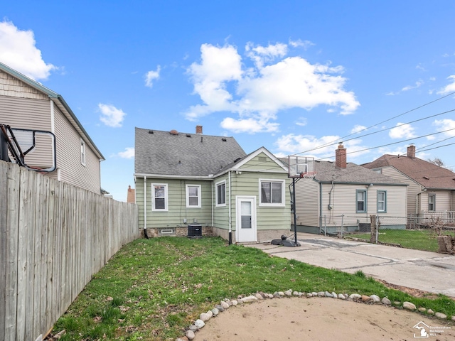 rear view of property featuring a fenced backyard, a shingled roof, central AC, and a yard