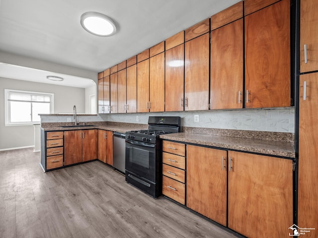 kitchen featuring stainless steel dishwasher, gas stove, a sink, light wood-type flooring, and a peninsula