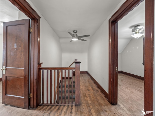 hallway featuring baseboards, vaulted ceiling, an upstairs landing, and wood finished floors