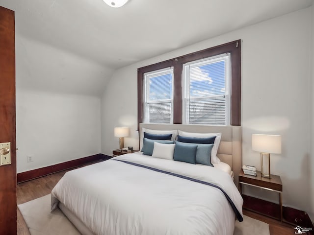 bedroom featuring lofted ceiling, baseboards, and wood finished floors