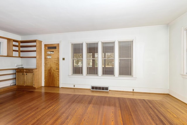 empty room with ornamental molding, visible vents, baseboards, and wood finished floors