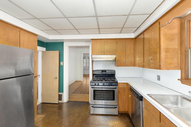 kitchen with under cabinet range hood, a sink, light countertops, appliances with stainless steel finishes, and brown cabinets