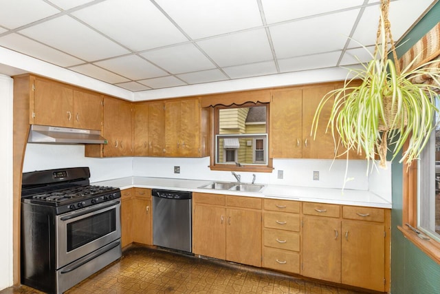 kitchen featuring light countertops, appliances with stainless steel finishes, brown cabinetry, a sink, and under cabinet range hood