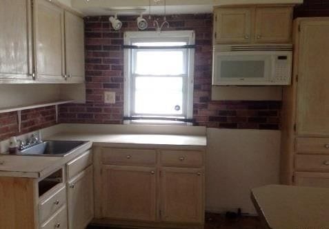 kitchen featuring white microwave, brick wall, light countertops, and a sink