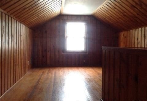 bonus room with vaulted ceiling, light wood finished floors, and wooden walls