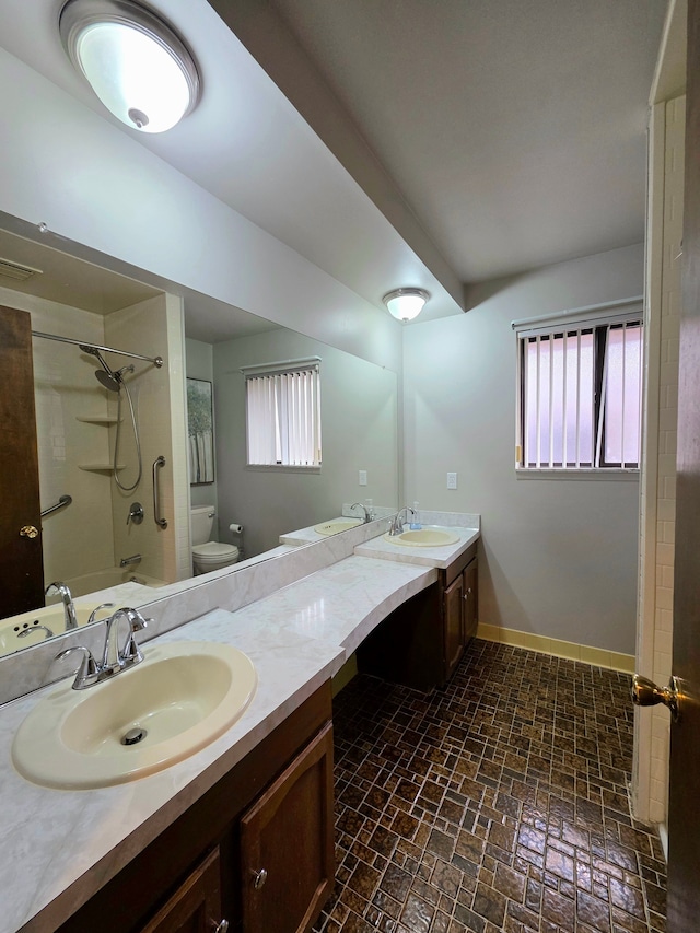 bathroom with toilet, double vanity, baseboards, and a sink