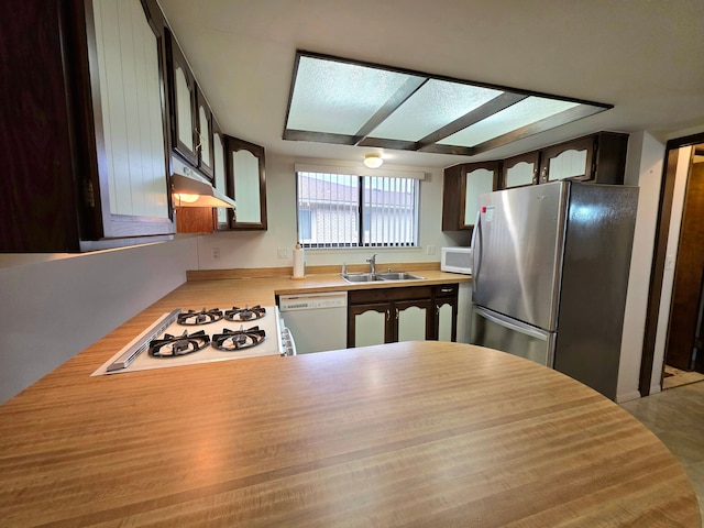 kitchen with white appliances, a peninsula, light countertops, under cabinet range hood, and a sink