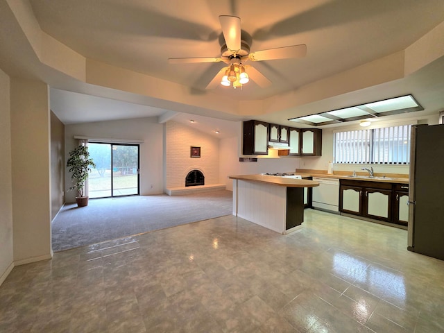 kitchen with freestanding refrigerator, a brick fireplace, vaulted ceiling, a sink, and dishwasher