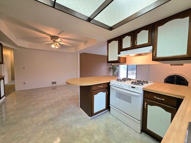 kitchen featuring white range with gas cooktop, a raised ceiling, a peninsula, light countertops, and under cabinet range hood