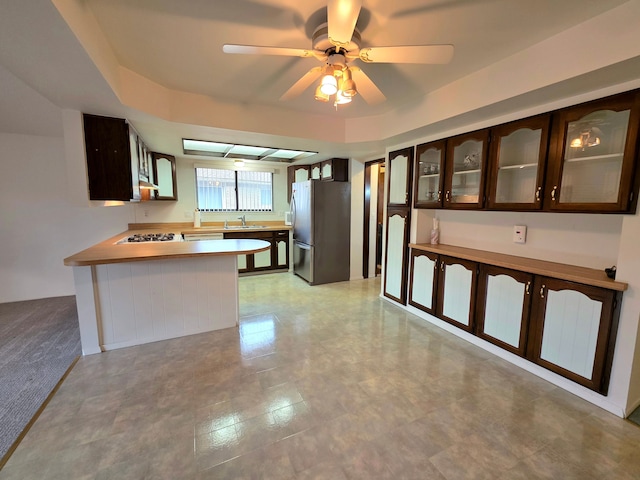 kitchen featuring dark brown cabinetry, glass insert cabinets, freestanding refrigerator, white gas cooktop, and a sink