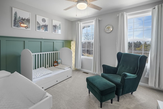 bedroom featuring a ceiling fan, visible vents, a crib, light carpet, and a decorative wall