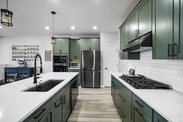 kitchen with black appliances, a sink, under cabinet range hood, green cabinets, and hanging light fixtures