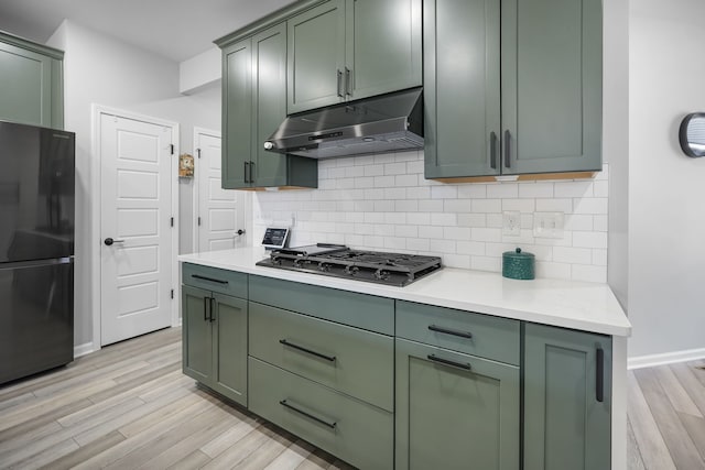 kitchen featuring under cabinet range hood, gas stovetop, freestanding refrigerator, and green cabinetry